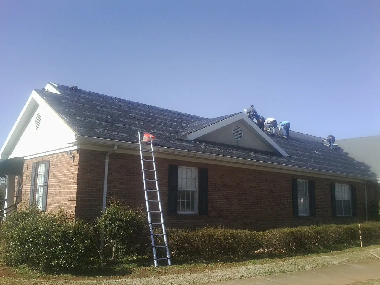 Crew tearing shingles off a brick ranch roof with a ladder set — Metal Roof Repair work by our crew in Achille