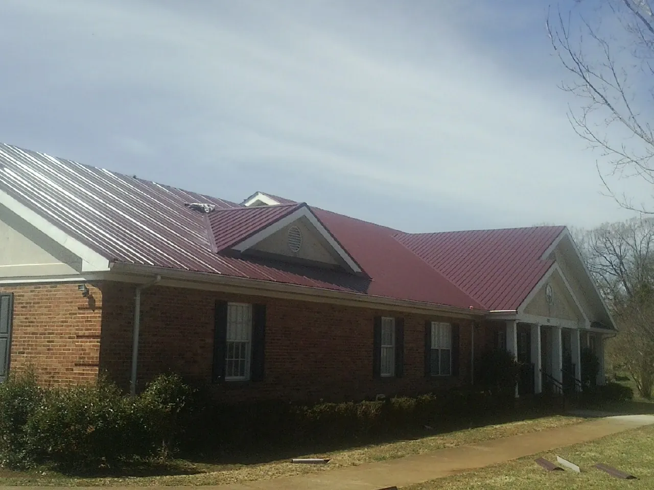 Red metal roof with gabled entries on a long brick building, from a Hail Damage Roof Repair job in Achille