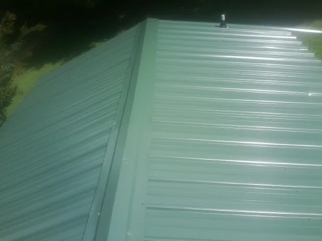New green metal panels meeting at the ridge of a roof — Flat Roof Repair work by our crew in Achille