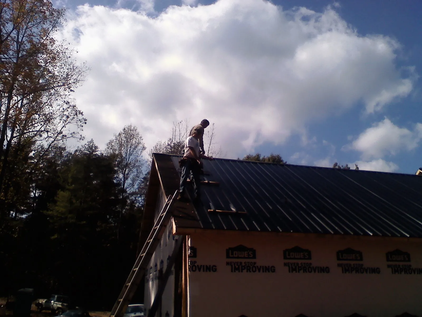Roofer fastening dark metal panels high against a cloudy sky, from a Roof Inspection job in Achille