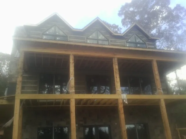 Dormers and porch framing on a large log home under construction — Roof Coating work by our crew in Achille