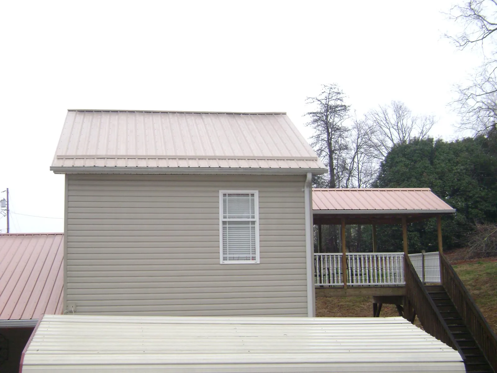 Tan metal roofs on a two story addition and attached porch, from a Roof Replacement job in Achille